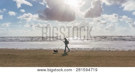 Man And His Dog Walking At The Beach At Sunset Or Sunrise.