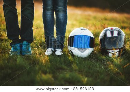 A Young Couple In Jeans Is Standing Next To Two Motorcycle Helmets