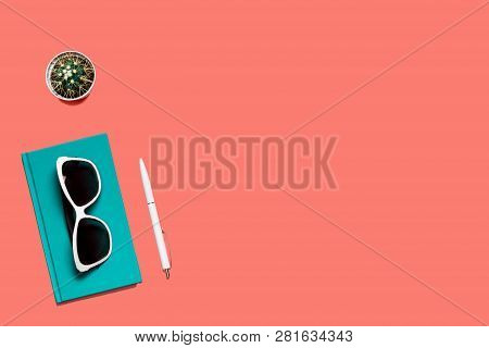 Trendy Colorful Flat Lay Composition. Coral Colored Desk With Turquoise Diary, White Glasses, Pen An