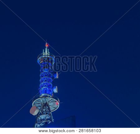 Low Angle Night View Of Large Communication Array Tower Lit Up In Blue Lights With Dark Blue Sky In 