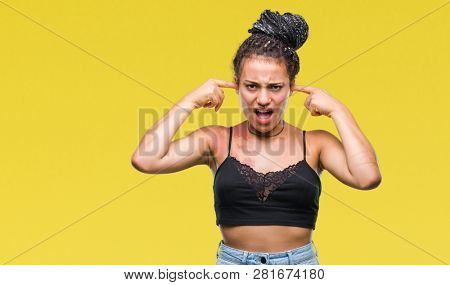 Young braided hair african american with pigmentation blemish birth mark over isolated background covering ears with fingers with annoyed expression for the noise of loud music. Deaf concept.