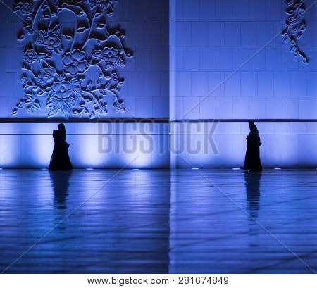 Silhouettes of muslims walking around the mosque wall in Grand Mosque, Abu Dhabi, UAE. Religious motive