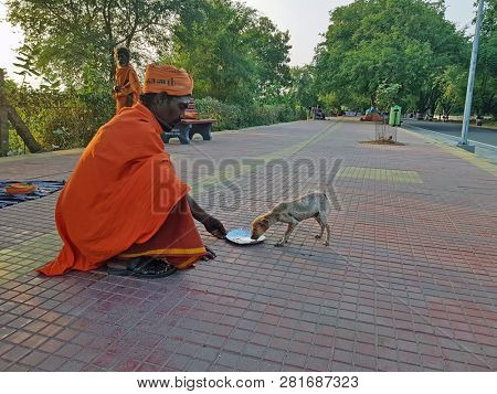 Tiruvanamalai, India - January 6, 2019: Sadhu feeding a baby dog with chai in India