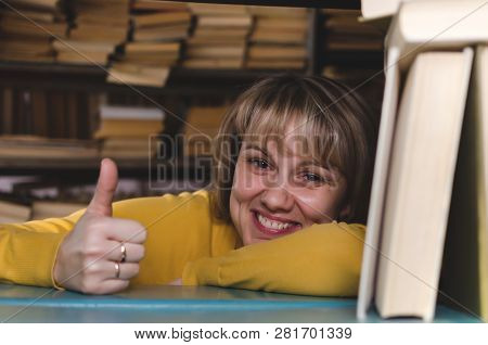 Happy Woman A Librarian Is Looking Through A Bookshelf In A Library And Is Showing A Thumbs Up.