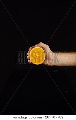 Half Of A Juicy Orange In Man's Hand On Black Background