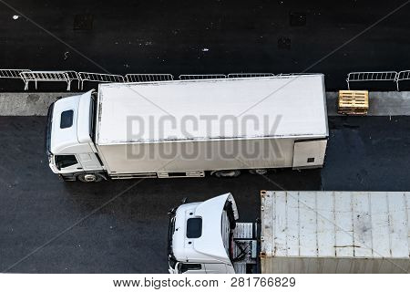Aerial/Overhead view of two white 6 wheeler delivery trucks parked side by side on asphalt road. Shipping/Delivery destination for goods.