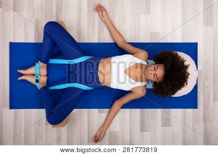 Relaxed Young Woman Lying On Fitness Mat Doing Exercise With Yoga Belt And Two Blocks