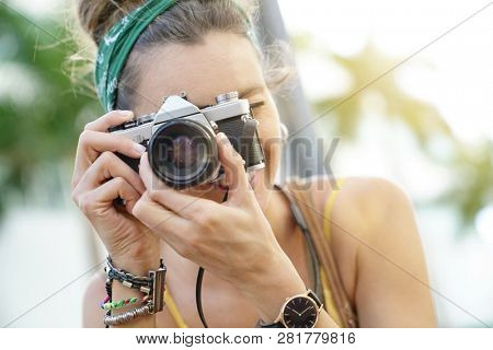 Portait of stylish young woman taking photos with vintage camera in urban setting