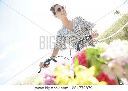 Gorgeous young woman in polka dot dress walking with bicylce on beach