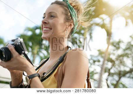 Stylish young woman taking photos with vintage camera surrounded by palm trees