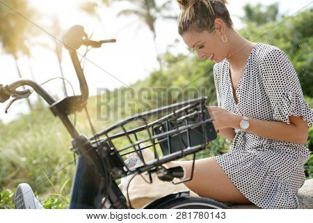 Pretty young woman sitting outdoors with bicylce and cellphone