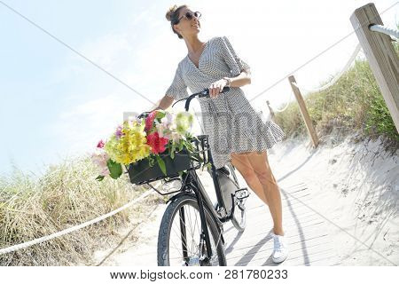 Gorgeous young woman in polka dot dress walking with bicylce on beach