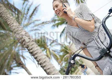 Pretty young woman sitting on bicycle outdoors talking on cellphone