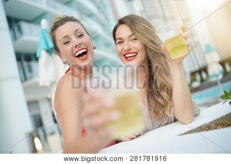 Two attractive funloving friends partying with drinks on rooftop bar in city