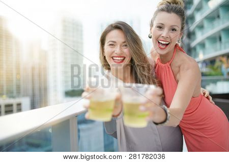 Two attractive funloving friends partying with drinks on rooftop bar in city