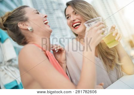 Two attractive funloving friends partying with drinks on rooftop bar in city