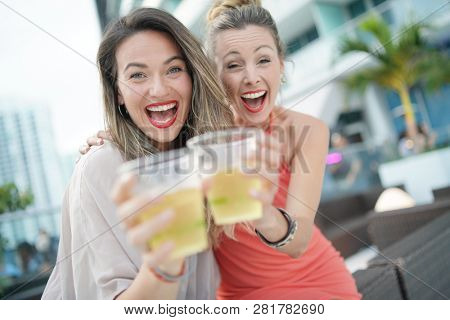 Two attractive funloving friends partying with drinks on rooftop bar in city