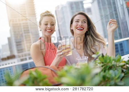 Two attractive funloving friends partying with drinks on rooftop bar in city
