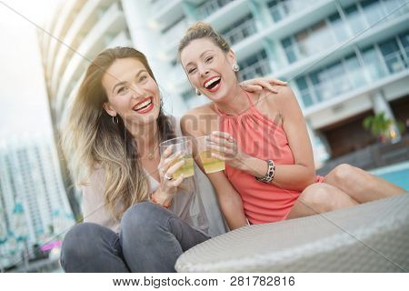 Two attractive funloving friends partying with drinks on rooftop bar in city