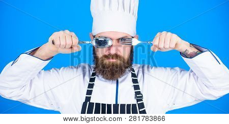 Chef Serious Strict Face Hold Spoon And Fork. Man Handsome With Beard Holds Kitchenware On Blue Back