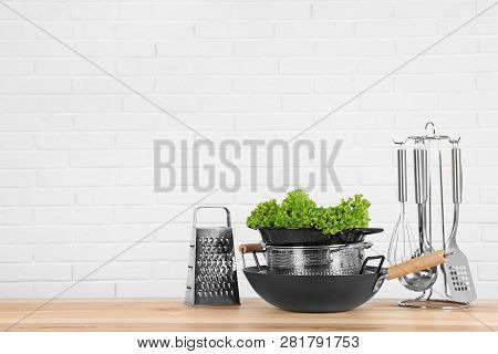 Set Of Clean Cookware, Utensils And Lettuce On Table Against  White Brick Wall. Space For Text
