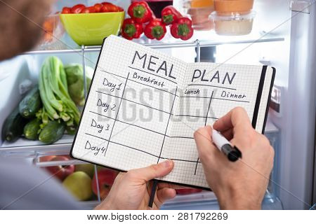 Person Writing On Notepad Near Refrigerator