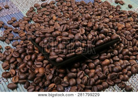A Scattering Of Coffee Beans On A Plate. Black Rectangular Plate. Bamboo Mat.