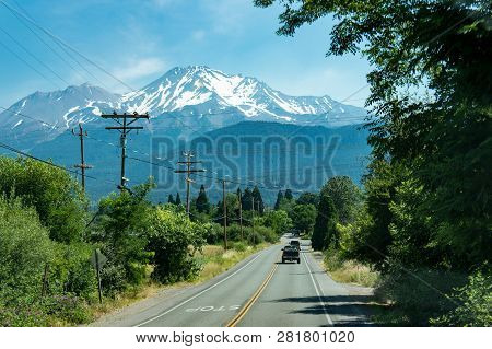 June 3 2017 - Mt. Shasta, California: A Car Drives Down The Tree Lined Road With Mt. Shasta, A Volca