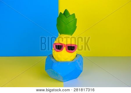 Funny Pineapple Toy In Concrete Pot  On Blue And Yellow Background