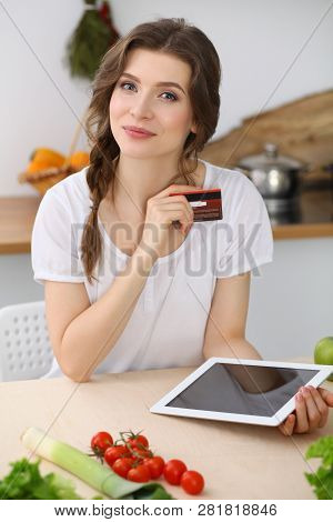 Young  Woman Looking For A New Recipe For  Cooking In A Kitchen. Housewife Is Making Online Shopping