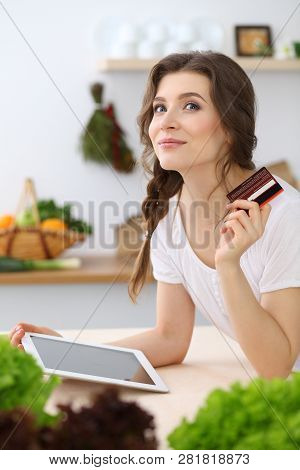 Young  Woman Looking For A New Recipe For  Cooking In A Kitchen. Housewife Is Making Online Shopping