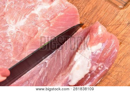 Cutting Pork Meat With A Black Knife, Close-up, On A Cutting Board. Pork Meat Ribs