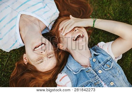 Friendship Is Miracle. Joyful And Carefree Cute Redhead Girls With Freckles, Lying On Green Grass An