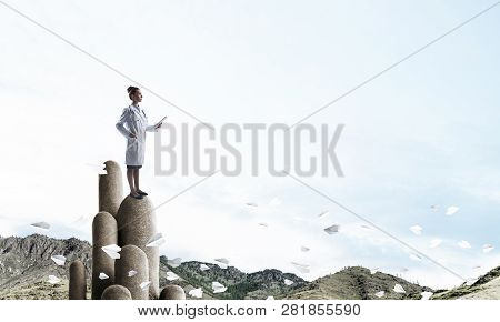 Young Female Doctor With Folder In Hands Satnding On Stone Column