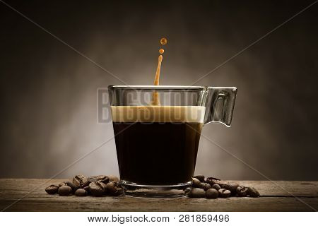 Black Coffee In Glass Cup With Coffee Beans And Jumping Drop, On Wooden Table