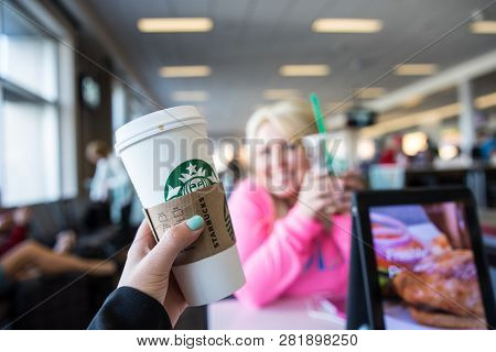 Minneapolis, Mn - May 2 2018: Hand Holds Up A Starbucks Coffee Drink At An Airport. Background Inten
