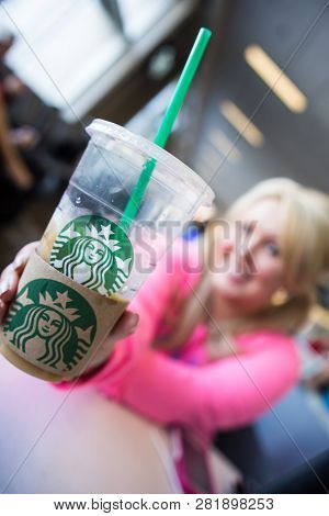 Minneapolis, Mn - May 2 2018: Blonde Female Holds Up A Starbucks Coffee Drink At An Airport. Intenti