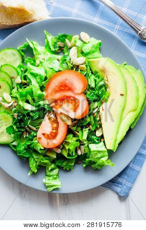Fresh  Green Salad With Cucumber, Lettuce, Avocado And Tomatoes And Glass Water On A White Wooden Ta