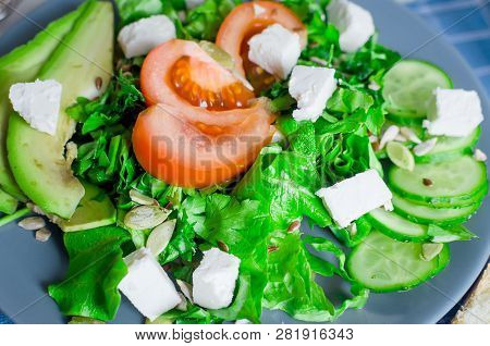 Fresh  Green Salad With Cucumber, Lettuce, Avocado, Tomatoes And Soft Cheese And Glass Water On The 