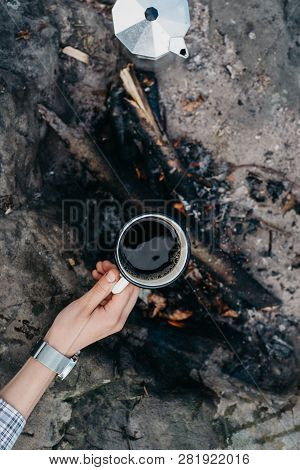 Girls Hand Holds A Hot Cup Of Coffee At The Background Of The Campfire. Concept Adventure Active Vac