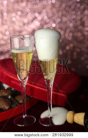 Valentines Day Champagne and Chocolates. Heart shaped velvet covered box of chocolates with roses and champagne with plastic champagne glasses. Room for text. 
