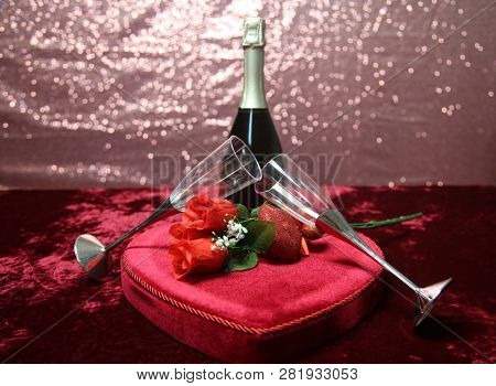 Valentines Day Champagne and Chocolates. Heart shaped velvet covered box of chocolates with roses and champagne with plastic champagne glasses. Room for text. 
