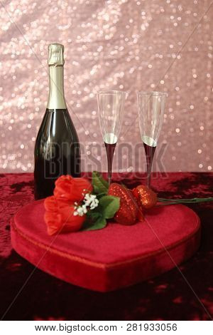 Valentines Day Champagne and Chocolates. Heart shaped velvet covered box of chocolates with roses and champagne with plastic champagne glasses. Room for text. 

