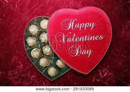 Valentines Day. Red Velvet Heart Shaped Valentines Day Chocolates Box.
On Burgundy Red Velvet background.  Text reads, Happy Valentines Day

