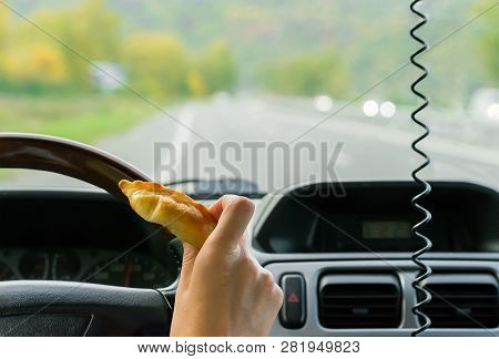 Closeup, Of Female Hand Holding A Bun Behind The Wheel Of The Car In Motion On Highway