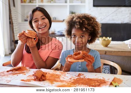 Two girlfriends having fun playing with modelling clay, holding up their creations and showing them to camera, close up
