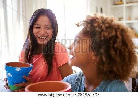 Laughing pre-teen girl and her older girlfriend holding plant pots that theyÃ¢â¬â¢ve decorated with paints at home, selective focus, close up