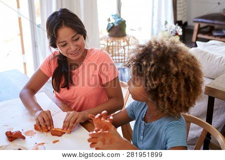 Two young teen and pre-teen girlfriends sitting at a table at home playing with modelling clay, close up, elevated view