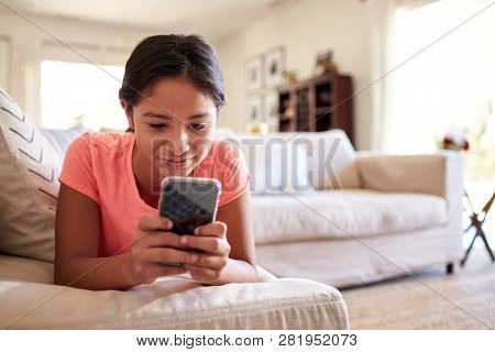 Teenage girl lying on the sofa at home in the living room using smartphone, close up, low angle, close up