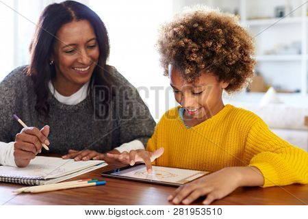 Mixed race young grandmother sitting at table doing homework with her granddaughter using a tablet computer, close up